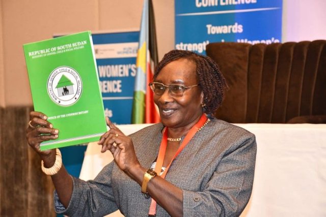 Woman holds up a green report with the words "Ministry of Gender, Child and Social Welfare" printed on the front