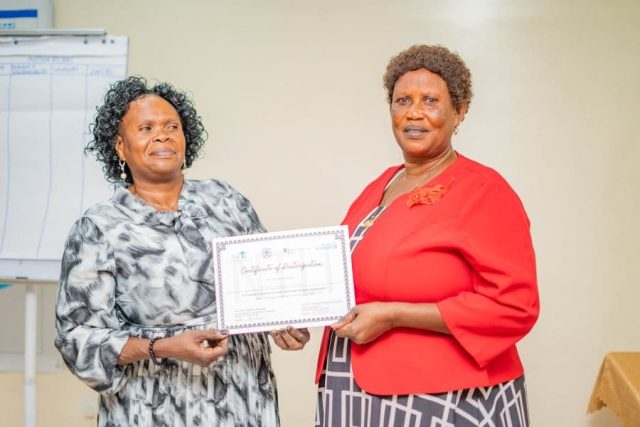 Two women look at the camera and pose for a photo, one is passing a certificate to the other