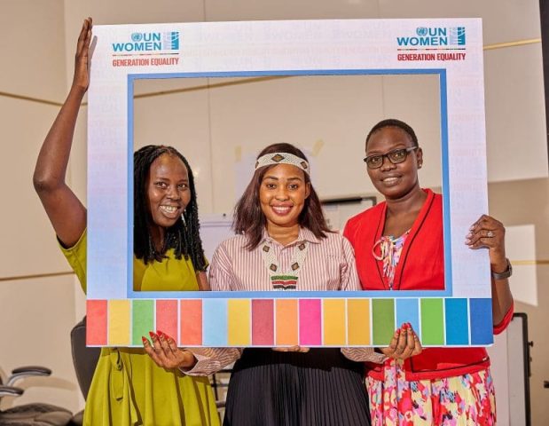 Three women appear through a cardboard cut out frame with the words "UN Women: Generation Equality" written on it